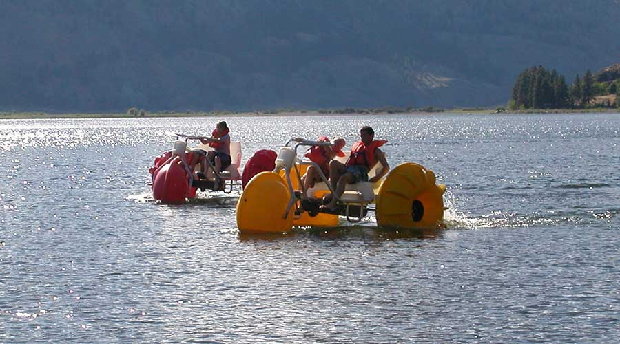 Environmentally friendly yellow and red Aqua-Cycle™ Water Trikes at a lake resort or youth camp rented for good profits by a recreational water equipment rental business.